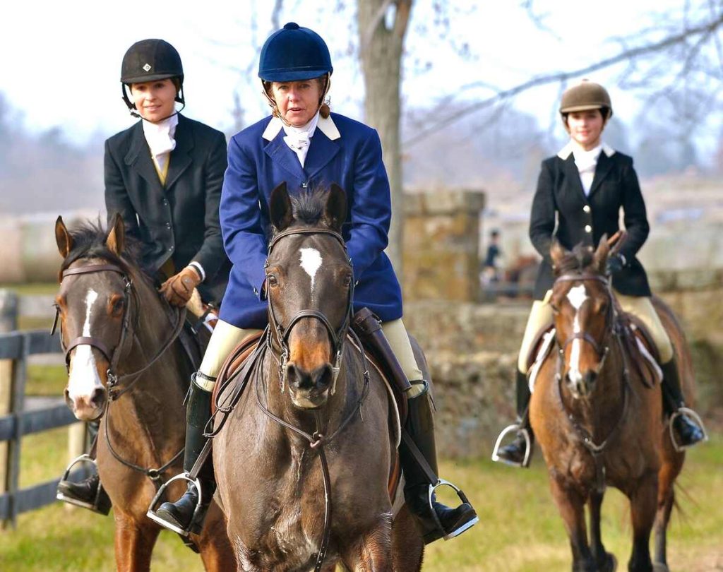 three women in formal hunt attire riding horses