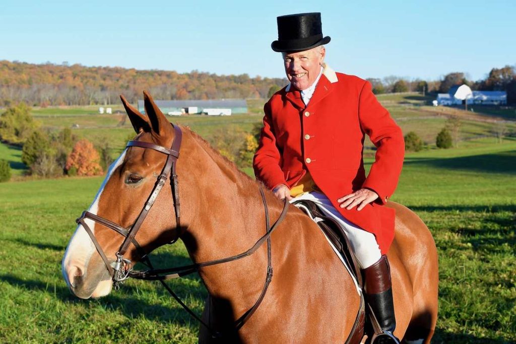 Max Tufts at Clovercroft, smiling man in red hunt coat and derby riding braided horse.