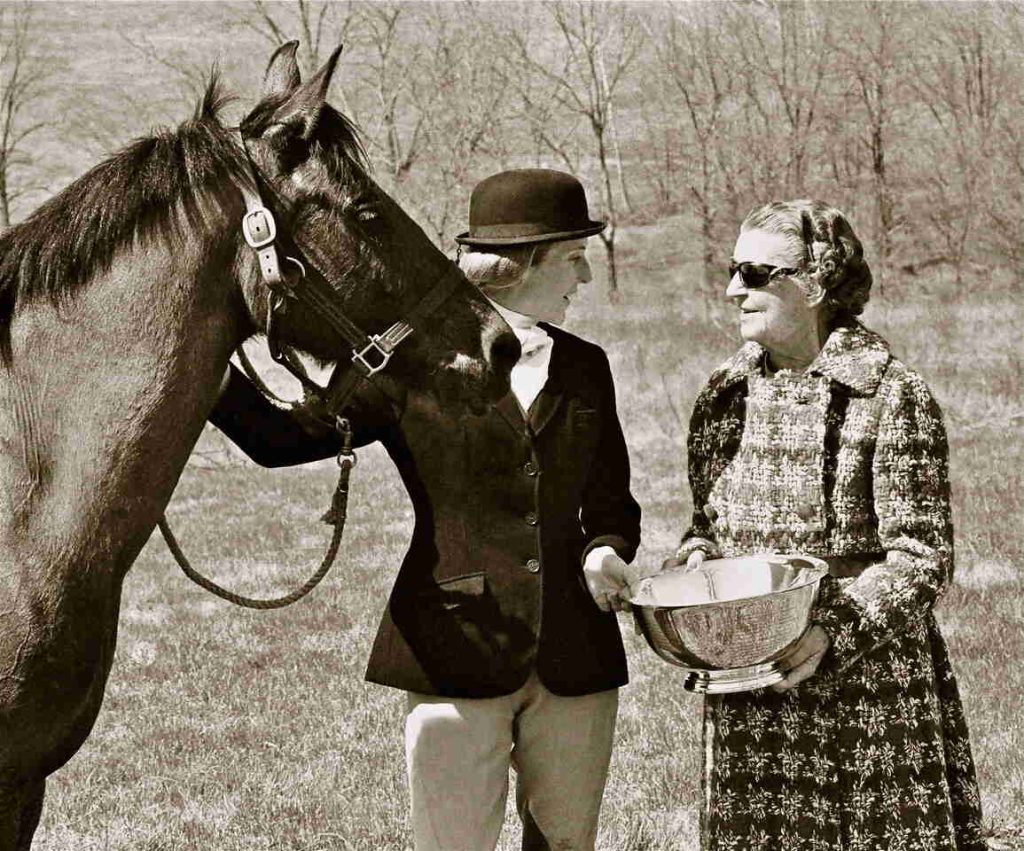 Woman presenting trophy to woman in hunt attire holding horse