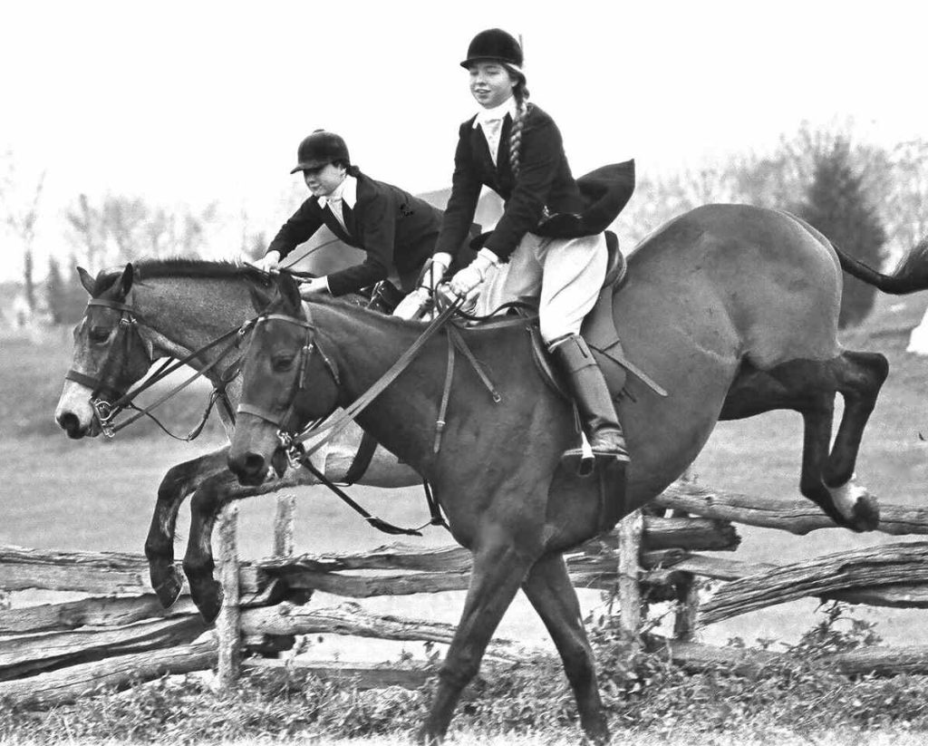two young ladies riding hunt horses over fences